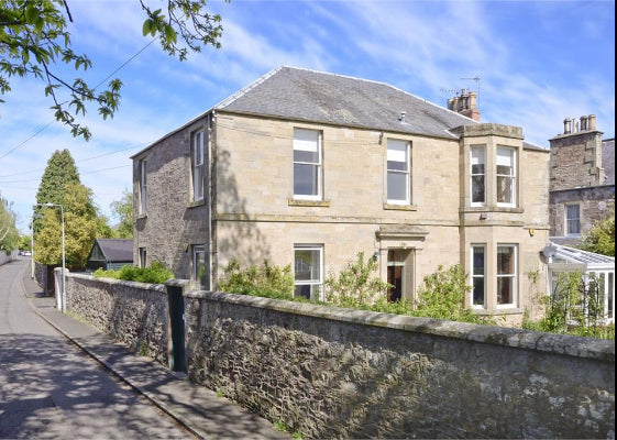 Two-story house with a stone wall and trees on a sunny day